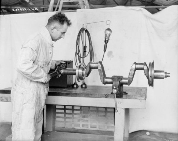 A man wearing a work coverall is working on machine parts. In the background is a white backdrop.