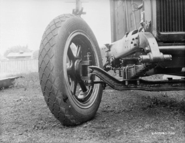 Close-up from front of the right wheel and axle of a Farmall tractor parked outdoors on grass. The tires are Goodyear.