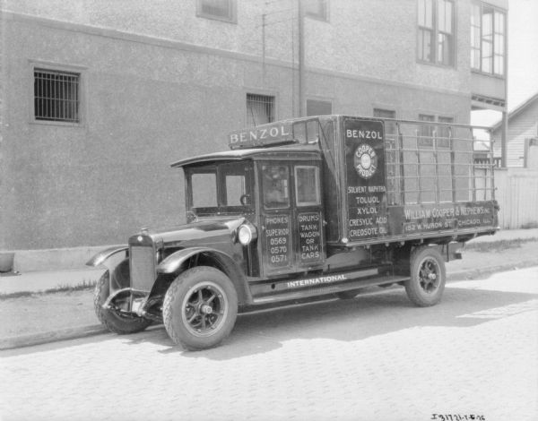 View across cobblestone street towards a delivery truck parked at the curb near a large building. There are signs on the truck, which read, in part: "Benzol," "Cooper Guaranteed Product," and along the side of the truck wagon, "William Cooper & Nephew, 152 Huron St., Chicago, Ill." 