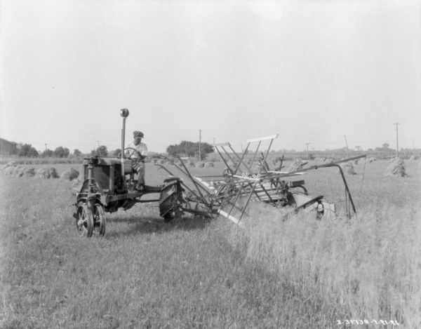 View across field towards a man driving a Farmall tractor to pull a harvester-thresher.