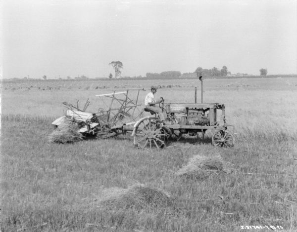 Right side view of a man using a Farmall tractor to pull a binder in a field.
