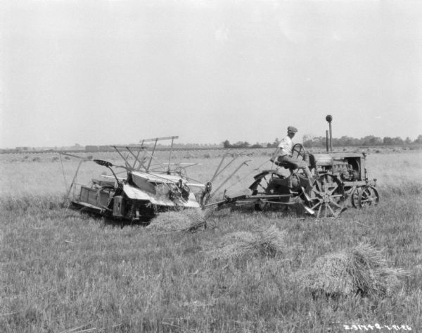 View across field towards a man using a Farmall tractor to pull a binder.
