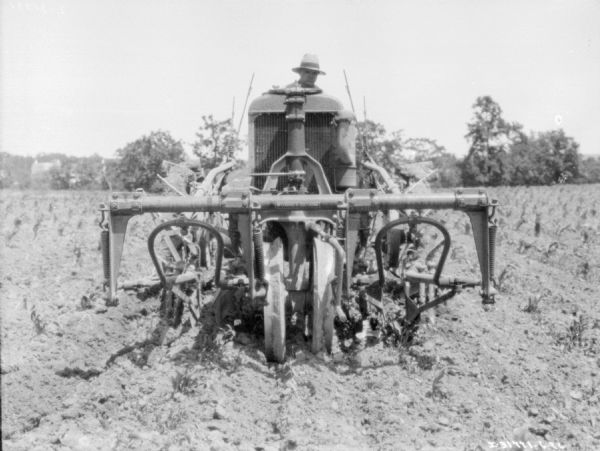 View from front of a man using a 10-20 tractor with a cultivator attached to work in a field.