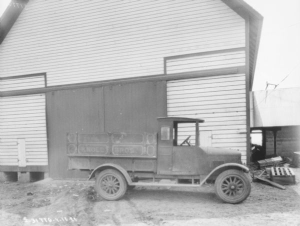 View of a truck parked alongside a barn. A faded sign on the side of the truck bed reads: "Knoll Bros."