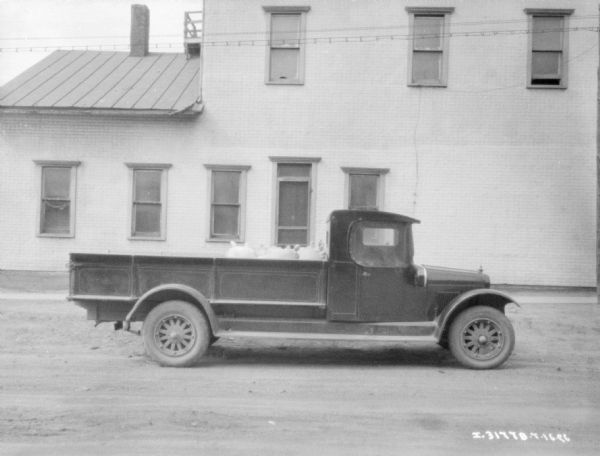 Right side profile view of a farm truck, with sacks in the truck bed. In the background is a brick building.