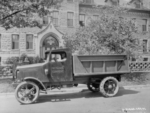 View across street towards a man sitting in the driver's seat of a truck in front of a church building. The sign painted on the driver's side door reads: "St. Francis Convent."