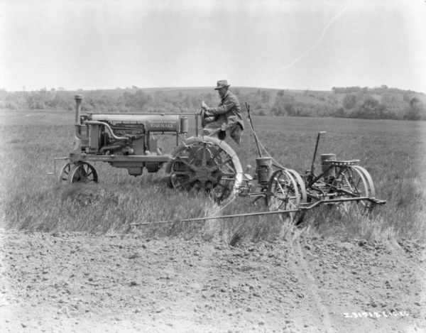 Left side profile view of a man using a Farmall tractor to pull a planter in a field.