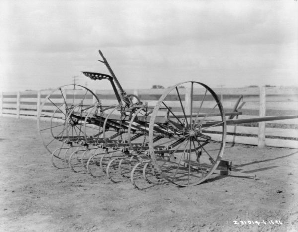 Cultivator parked in a field near a fence.