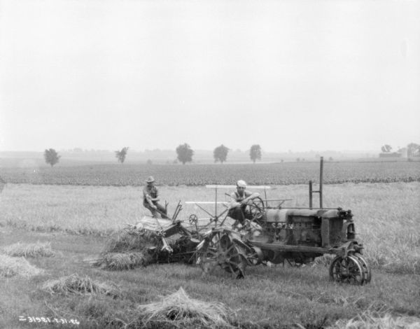 Right side view of two men in a field. One of the men is sitting on a Farmall tractor pulling the binder. The other man is sitting on the binder.