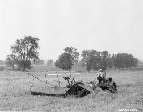 Three-quarter view from right rear of a man using a tractor drawn binder in a film.