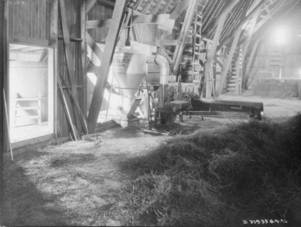 View across pile of hay towards a grain mill in a barn.