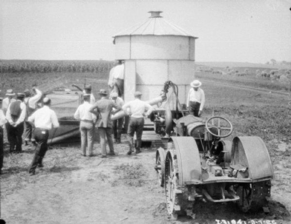Elevated view of a threshing operation. Men are standing near a tractor and a small, round farm building, perhaps a crib for drying corn.