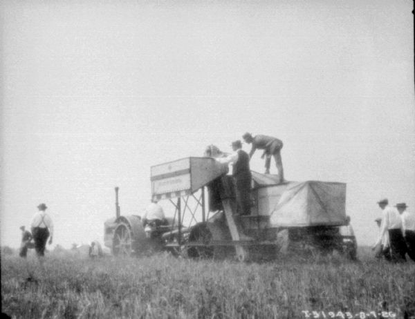 View across field towards demo of new machine(?) with a crowd of well-dressed men observing.