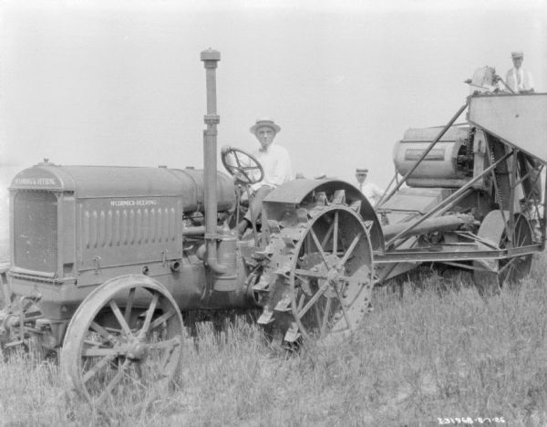 Group portrait of a man driving a McCormick-Deering tractor, and men standing behind him in a field. There is a man standing high up on the back of the harvester thresher.