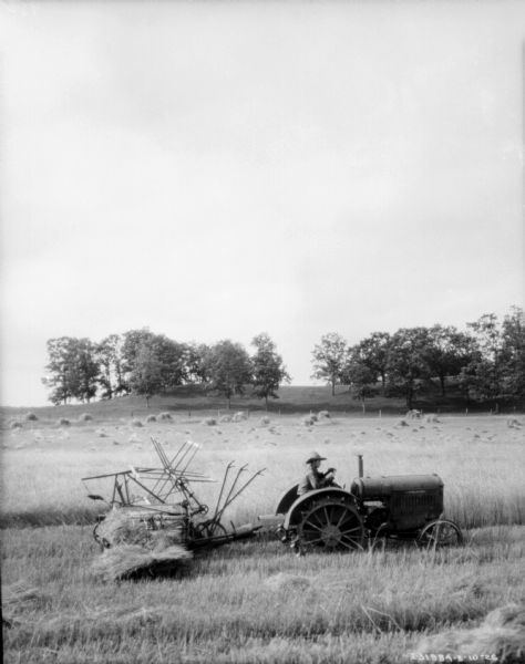 Slightly elevated view of a man driving a tractor pulling a binder in a field.