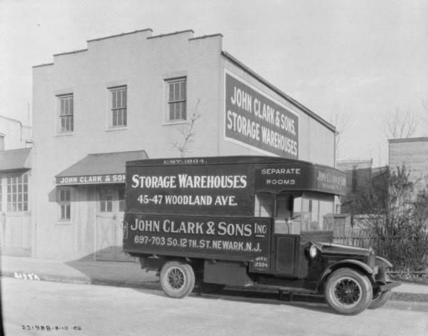 A moving van is parked along the curb in front of a building with signs that read: "John Clark & Sons, Storage Warehouses."