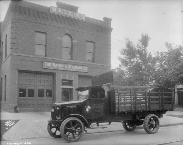 View across street towards an International delivery truck parked in front of the Watkins Beverage Co. building.