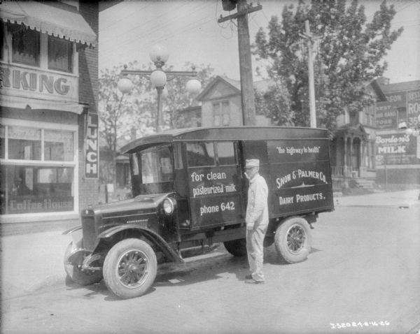 View across street towards a man standing on the side of a Snow & Palmer Co. delivery truck. Signs on the side of the truck read: "for clean pasteurized milk" and "the highway to health."
