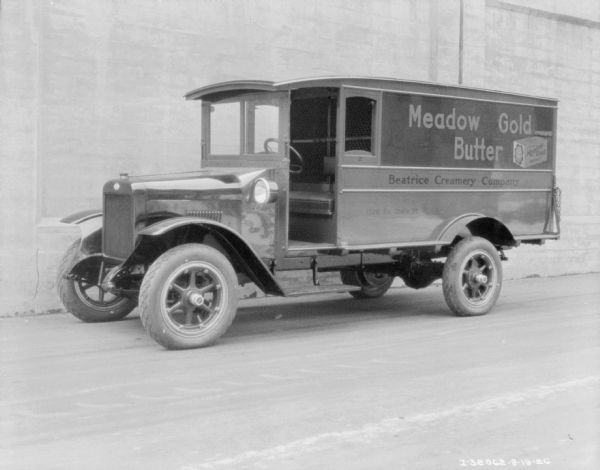 View across street towards a dairy delivery truck parked along the side of a building. The sign painted on the truck reads: "Meadow Gold Butter" and "Beatrice Creamery Company."