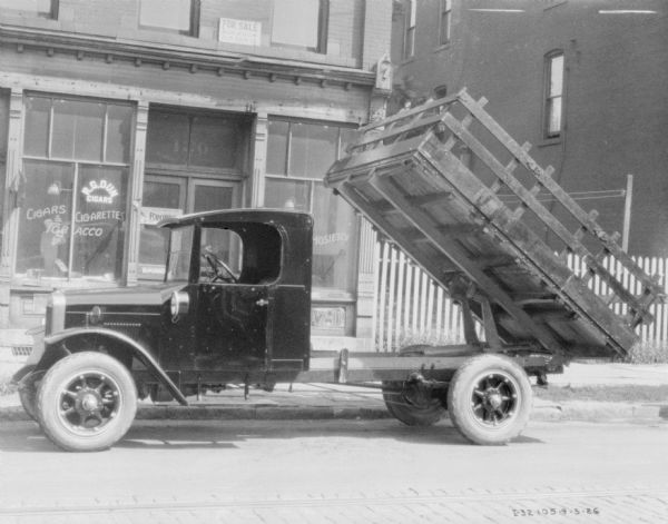 View across street towards a coal delivery truck parked at the curb in front of the R.G. Dun tobacco store. The truck bed is raised.
