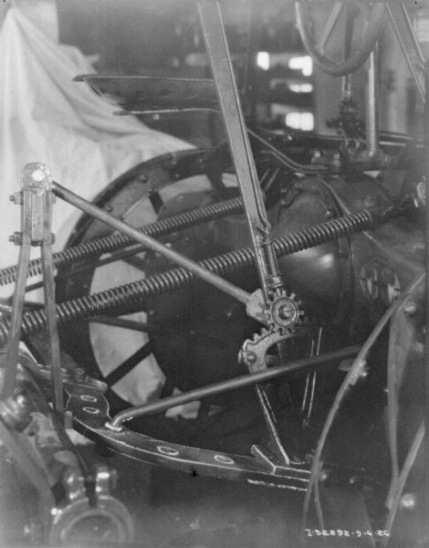 Close-up of parts on a cultivator. The cultivator is attached to a tractor on the right.