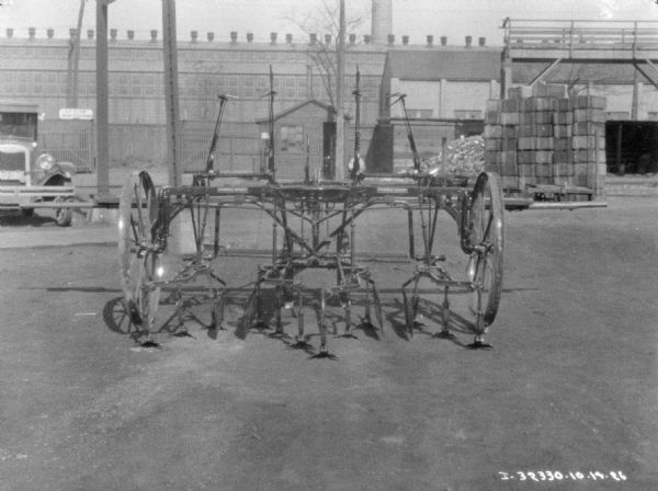 Cultivator set up in the yard of a factory. There is an automobile in the background on the left.