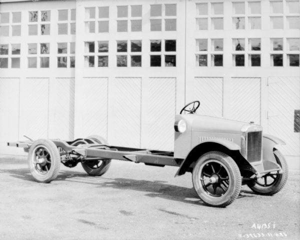 Three-quarter view from front right of a truck with an exposed chassis parked in front of a garage, with the doors closed.