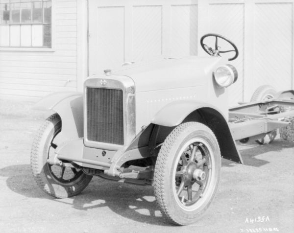 Three-quarter view from front left of a truck with exposed chassis parked outdoors in front of a garage with the doors closed.