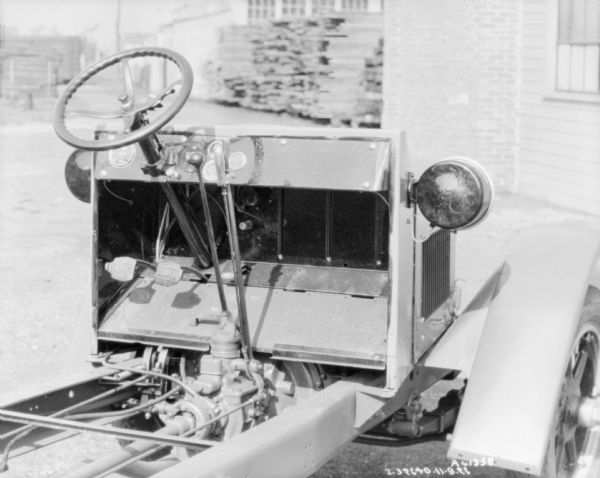 Three-quarter view from right of the steering wheel, gas and brake pedals, gear stick and shift assembly mounted on the exposed chassis.