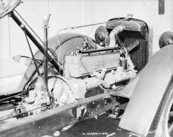 Close-up of engine, steering wheel, gas and brake pedals, gear stick and shift assembly on the exposed chassis.