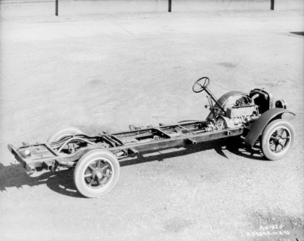 Slightly elevated view of truck with exposed chassis. The engine, steering wheel, and shift assembly is exposed in front, there is a front grill and fenders over the front wheels.