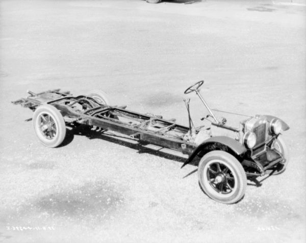 Slightly elevated view of truck with exposed chassis. The engine, steering wheel, and shift assembly is exposed in front, there is a front grill and fenders over the front wheels.