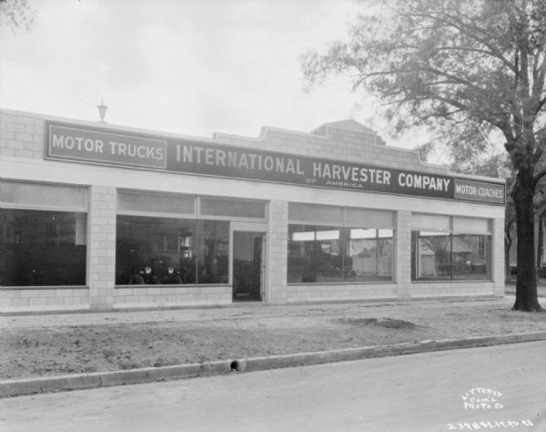 View across street towards an IHC Motor Truck dealership. Automobiles are on display behind large display windows.