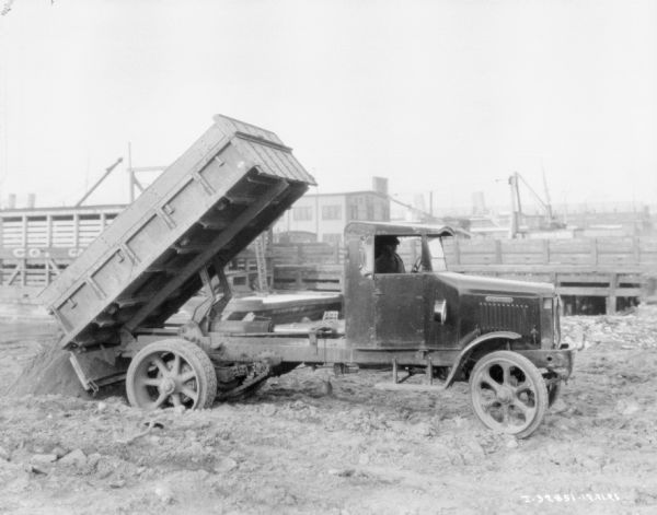 A man sitting in the cab of a delivery/dump truck. The bed of the truck is tipped while unloading material.