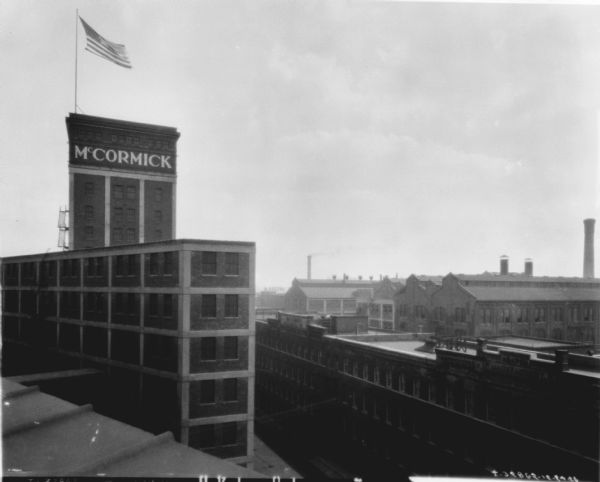 Elevated view from roof of new plant addition and old "Reaper Manufactory." A flag is flying from a pole on the roof of a brick building on the left, which has a sign that reads: "McCormick."