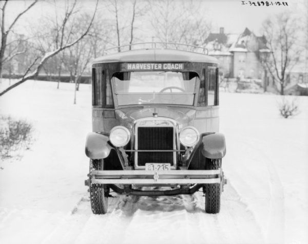 View of front of truck with a sign above the front window that reads: "Harvester Coach." There is a large building in the background. Snow is on the ground.
