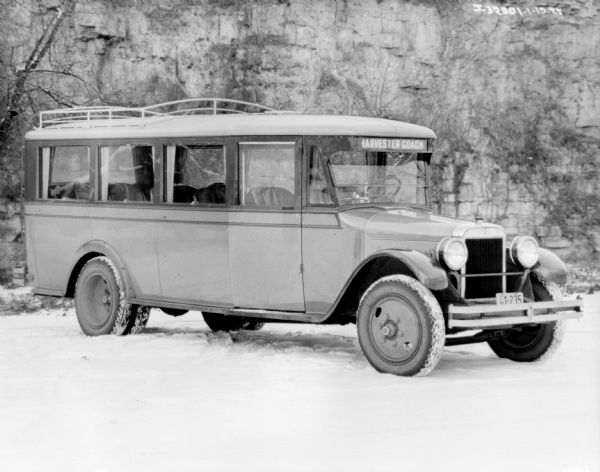 Three-quarter view from front right of a truck with a sign above the front window that reads: "Harvester Coach." Large windows are on the sides and back of the vehicle. Snow is on the ground.