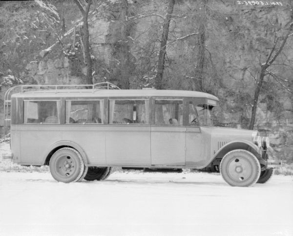 Three-quarter view from front right of a truck with a sign above the front window that reads: "Harvester Coach." Large windows are on the sides and back of the vehicle. Snow is on the ground.