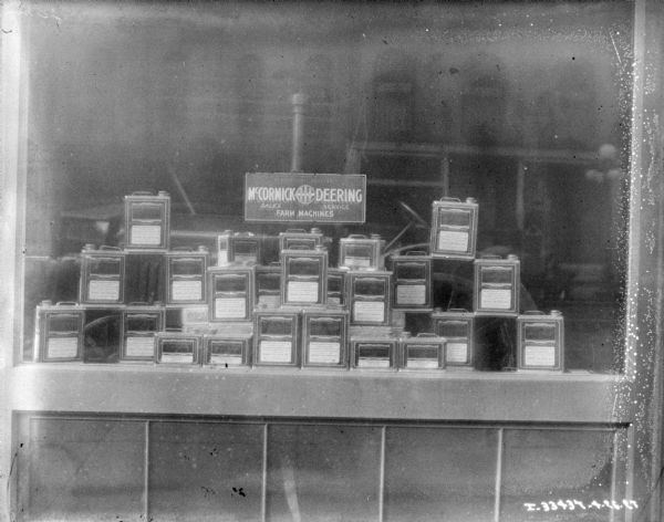 View of a display window of motor oil at a dealership. A sign in the background reads: "International Harvester, McCormick-Deering, Sales, Service, Farm Machines."