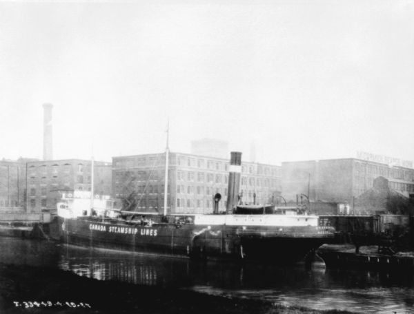 View from shoreline across a canal towards a Canada Steamship Line ship docked at McCormick Works.