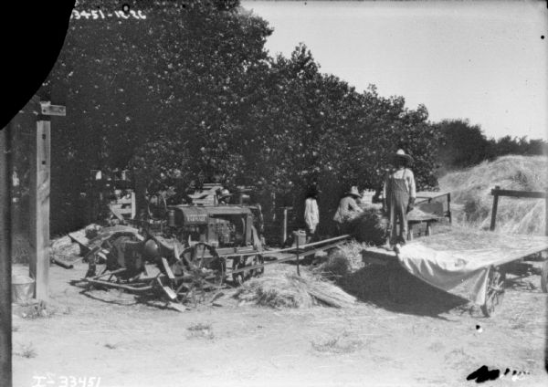 A group of men are working in a field with machinery being belt-driven with a Farmall tractor.