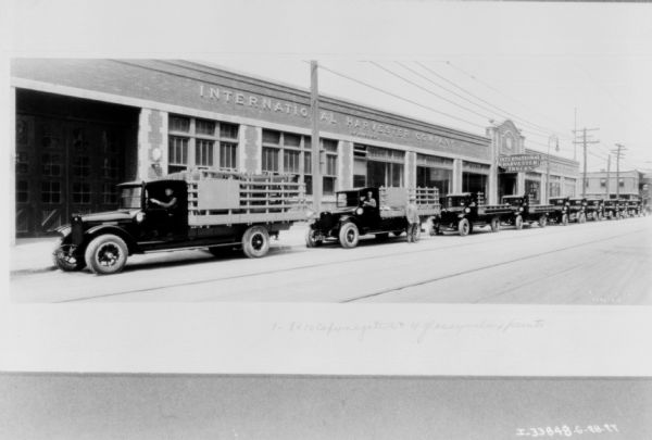 View across street towards a long line of delivery trucks along the curb in front of an IH dealership.