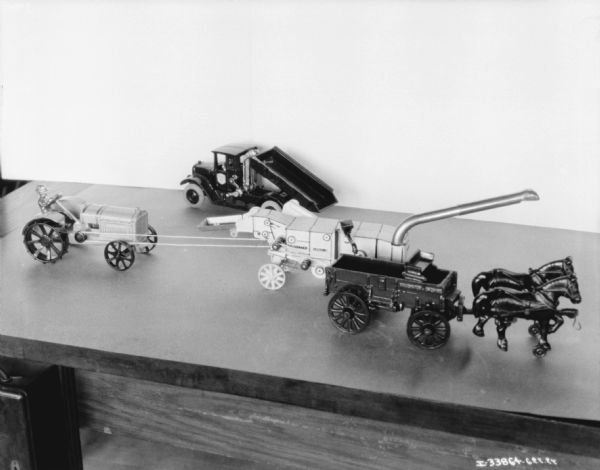 Group of miniature models on a table. The models include a dump truck, tractor, wagon, and harvester-thresher.