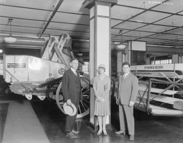 Two men and a woman are posing in the showroom of a dealership. Behind them is a McCormick-Deering harvester-thresher.