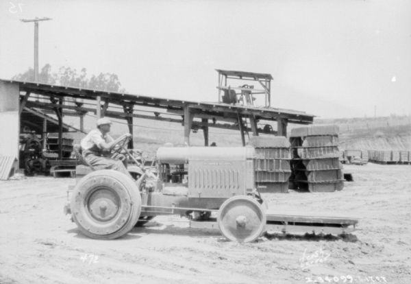 A man using a McCormick-Deering industrial tractor to move a load of bricks in a warehouse yard.