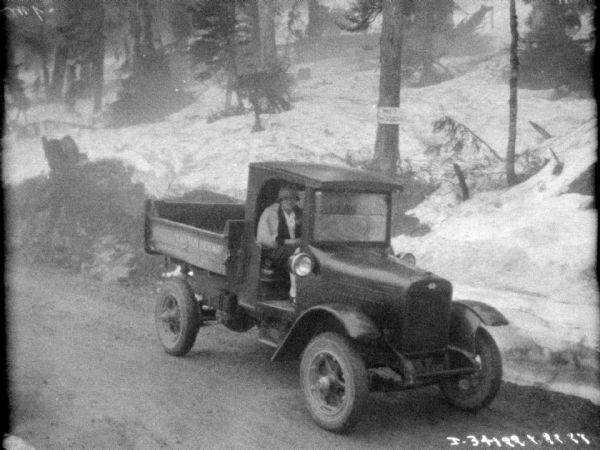 Elevated view of a woman sitting in the passenger seat in the cab of a truck. Trees are on the snow-covered hill in the background.