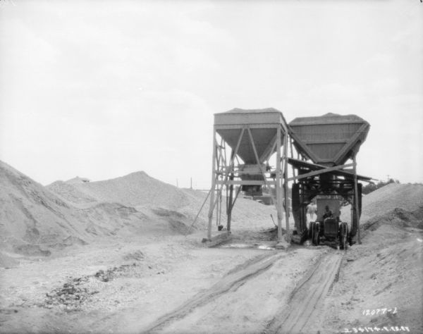 Men driving tractors pulling trailers, which are being loaded from a hopper at a granite quarry or mine.
