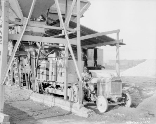 Man driving tractor pulling a trailer, which are being loaded from a hopper at a granite quarry or mine.