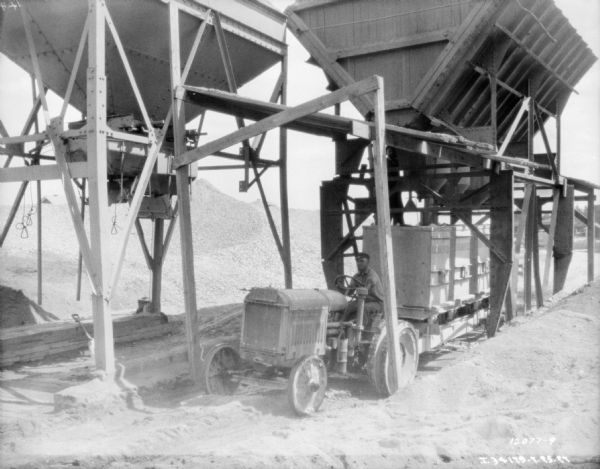 Slightly elevated view of a man driving an industrial tractor pulling a tractor that is being loaded while under a hopper at a granite quarry or mine.