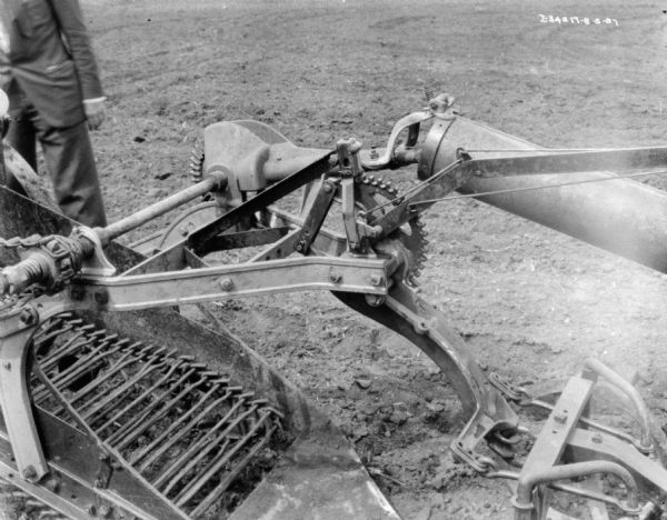 Close-up view looking down at a section of a potato digger. A man (his face out of frame) is standing in the upper right behind the machine. 